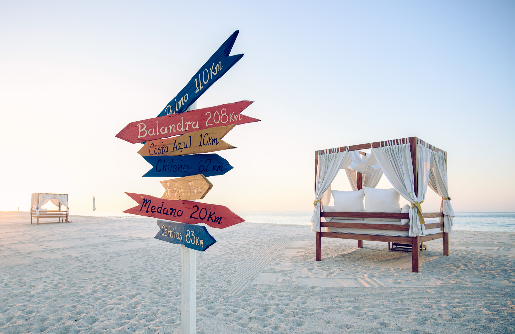 Kevin Steele - A signpost with travel destinations on a beach