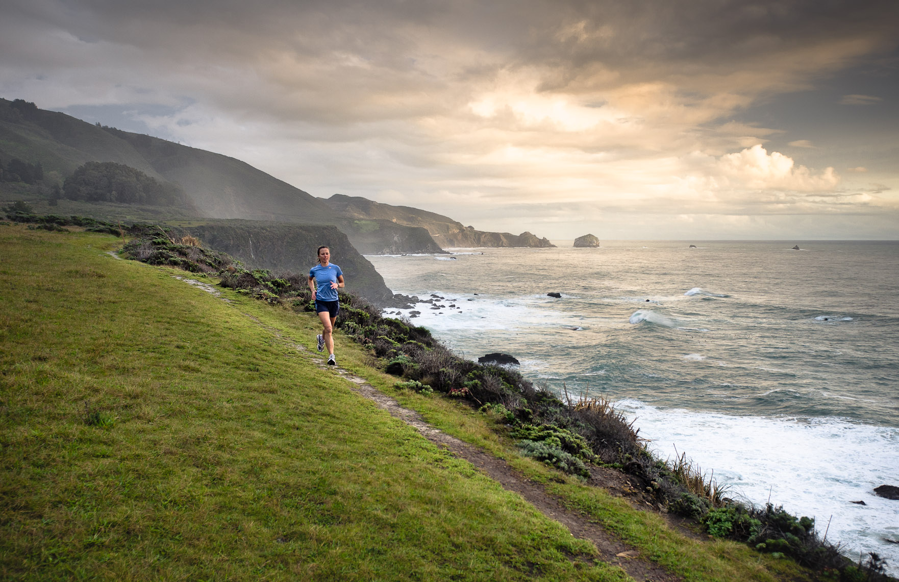 Kevin Steele - A young woman running along a cliff trail above the ocean
